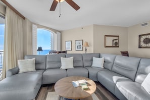 A spacious living room with a large gray sectional sofa, a round coffee table, and a ceiling fan.