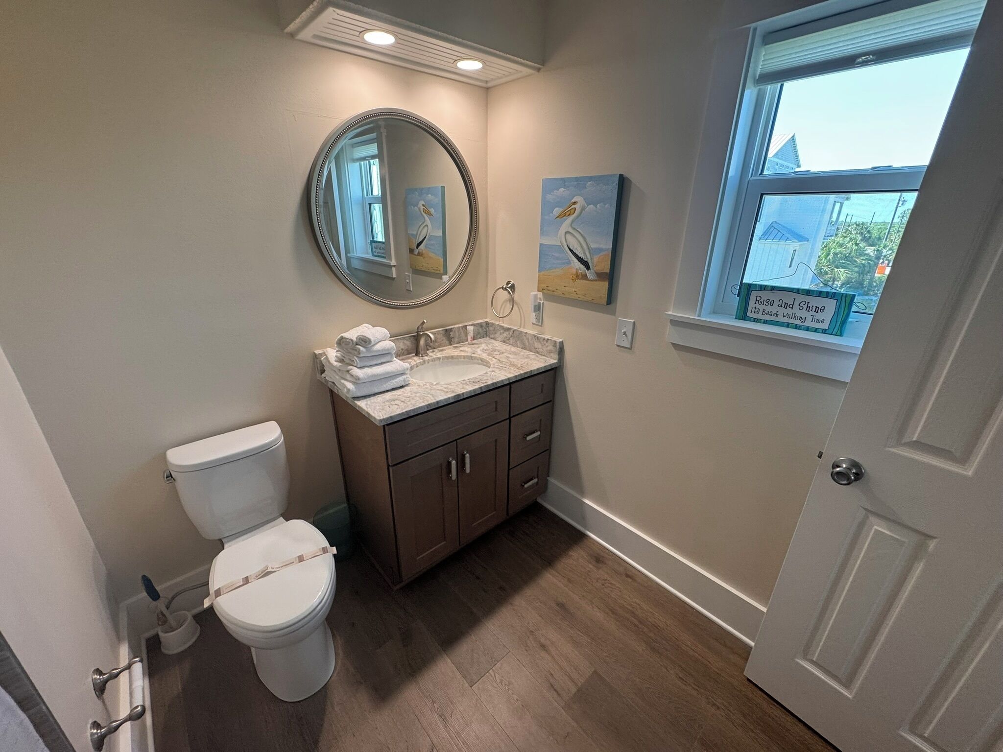 A bathroom with a toilet, sink, vanity, and a window with a view of the outside.