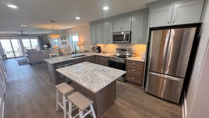 A modern kitchen with grey cabinets, stainless steel appliances, and a marble island with stools. - Fully Remodeled 2025 Beachfront Escape- Pet Friendly- Steps to Sand & Gulf Views (St Joe Beach)