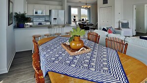 A modern kitchen with white cabinets, a dining area with a patterned tablecloth, and a living room with a sofa and chairs. - You’re The Tops | Oceanfront, Amazing Views! (Surf City)