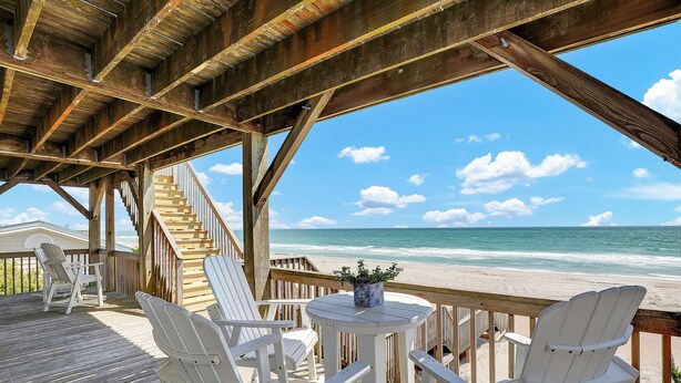 A wooden deck with white chairs and a table, overlooking a beach with a clear sky. - You’re The Tops | Oceanfront, Amazing Views! (Surf City)