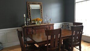 Ein Esszimmer mit Holztisch und -stühlen, einem Spiegel und einer Vase mit Blumen auf einer Kommode.