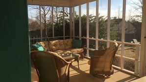 Eine überdachte Terrasse mit Korbmöbeln, einer Couch und einem Esstisch.