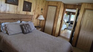 Een slaapkamer met een houten hoofdbord, een bed met beddengoed met een patroon, een nachtkastje met een lamp en een deur die naar een andere kamer leidt.