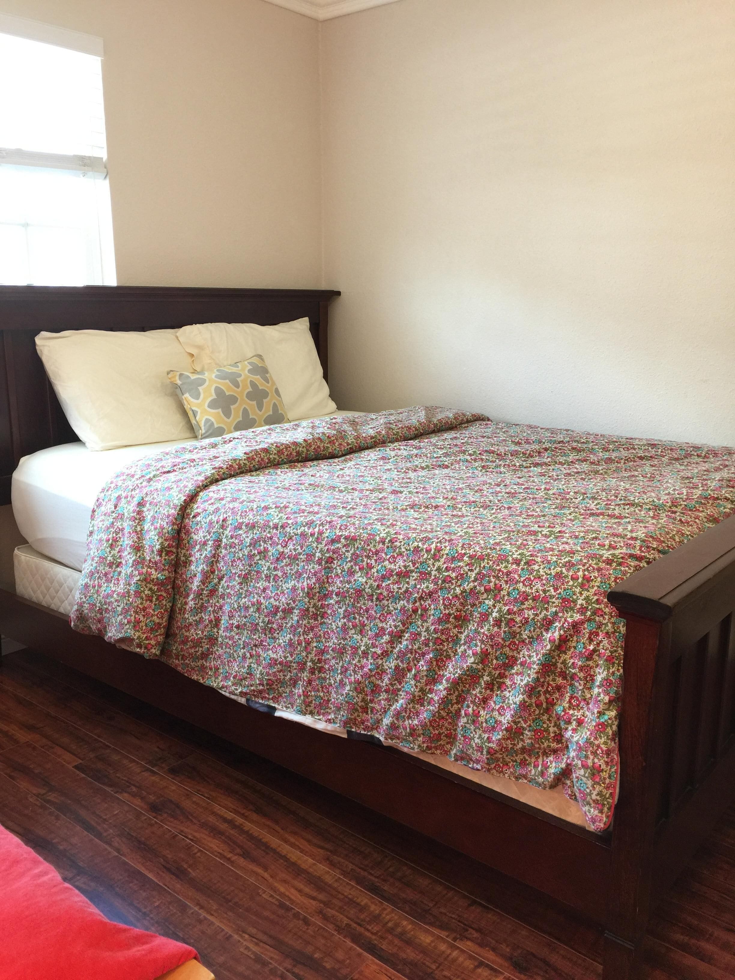 A single bed with a floral bedspread, a headboard, and two pillows.