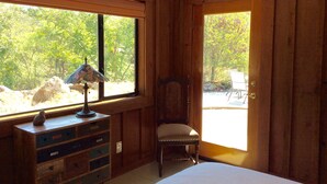 A room with wooden walls, a bed, a desk with a lamp, and a chair.