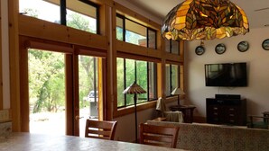 A kitchen with a large window, a dining area with a table and chairs, and a television mounted on the wall.