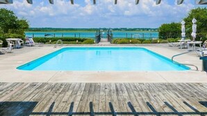Une piscine avec une terrasse en bois, des chaises longues et une vue sur l’océan.