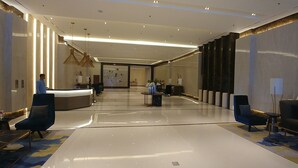 Un hall d’hôtel moderne avec un comptoir d’accueil, des espaces salon et un grand miroir.