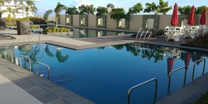 Piscina retangular com água azul cristalina, rodeada por um deck de madeira e grades de metal.