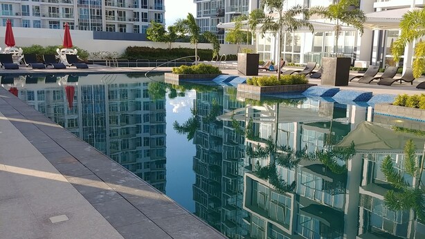 Un espace piscine moderne, avec des chaises longues, une eau cristalline et une végétation luxuriante tout autour.