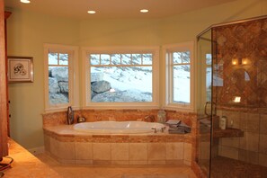 A bathroom with a large bathtub, a glass shower enclosure, and a view of a snowy landscape through three windows. - “Bella Vista” Overlooking Beautiful Flathead Lake with Great Panoramic Views! (Somers)