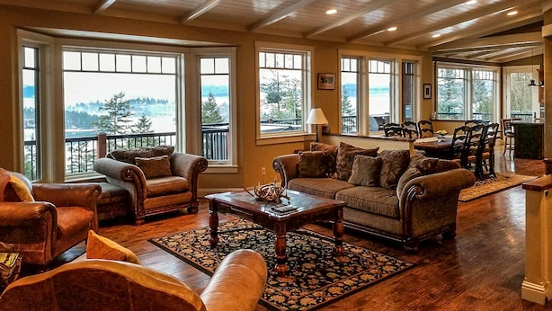 A spacious living room with large windows, a fireplace, and a dining area with wooden furniture. - “Bella Vista” Overlooking Beautiful Flathead Lake with Great Panoramic Views! (Somers)