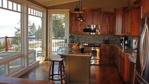 A spacious kitchen with wooden cabinets, a large island, and a view of the outdoors. - “Bella Vista” Overlooking Beautiful Flathead Lake with Great Panoramic Views! (Somers)