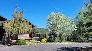 A house with a stone facade, a porch, and a large tree with white blossoms. - “Bella Vista” Overlooking Beautiful Flathead Lake with Great Panoramic Views! (Somers)