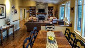 A spacious living room with a fireplace, comfortable seating, and a dining area with a table set for four. - “Bella Vista” Overlooking Beautiful Flathead Lake with Great Panoramic Views! (Somers)