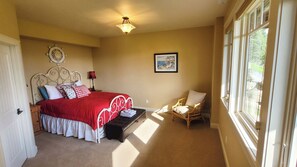 A bedroom with a bed, a chair, a window, and a painting on the wall. - “Bella Vista” Overlooking Beautiful Flathead Lake with Great Panoramic Views! (Somers)