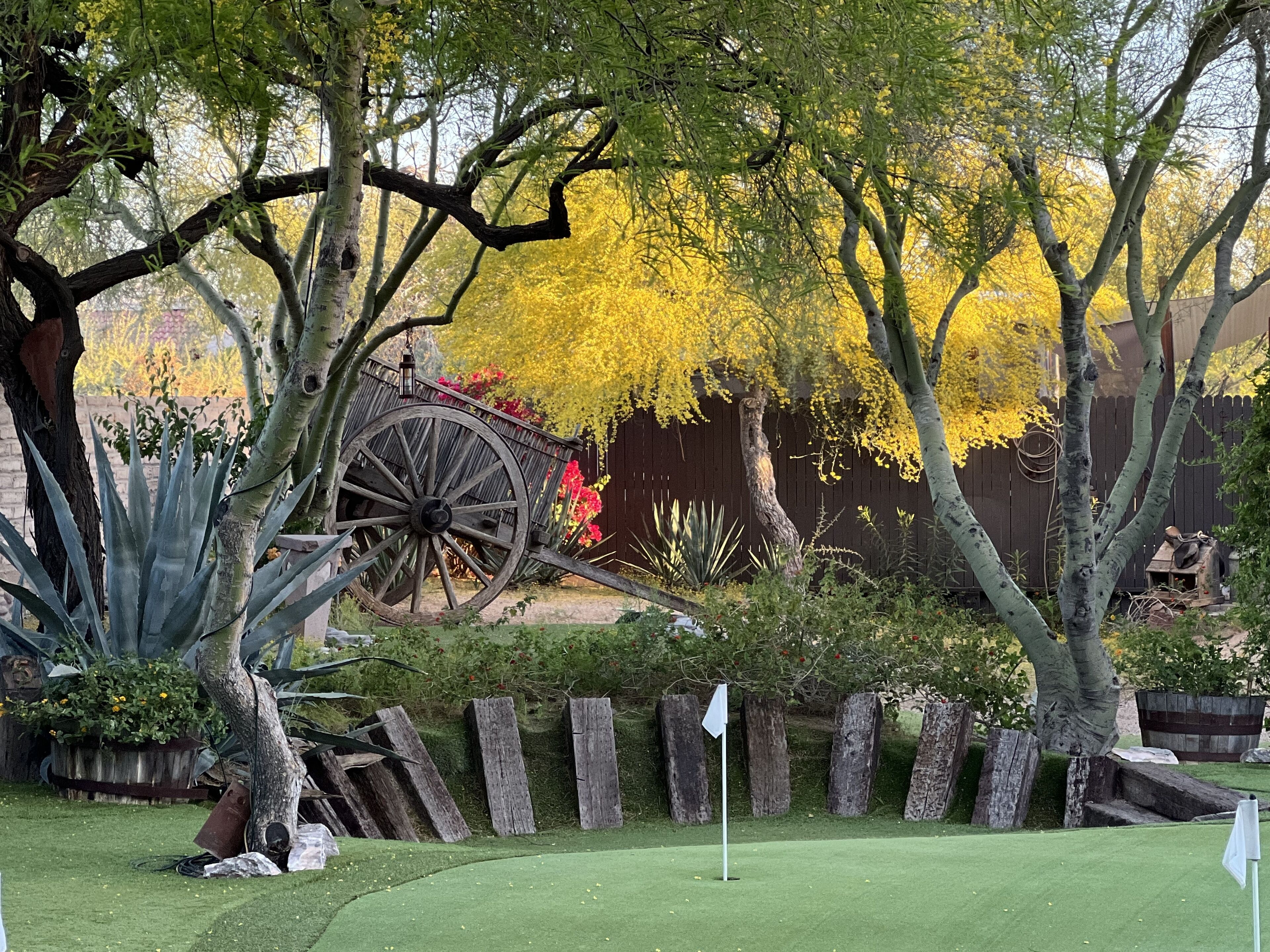 A golf course with a wooden cart, a flagstick, and a wooden fence.