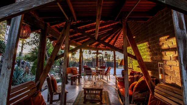 Eine Terrasse im Freien mit Holzmöbeln, einer Backsteinwand und einer Holzdeckenkonstruktion.