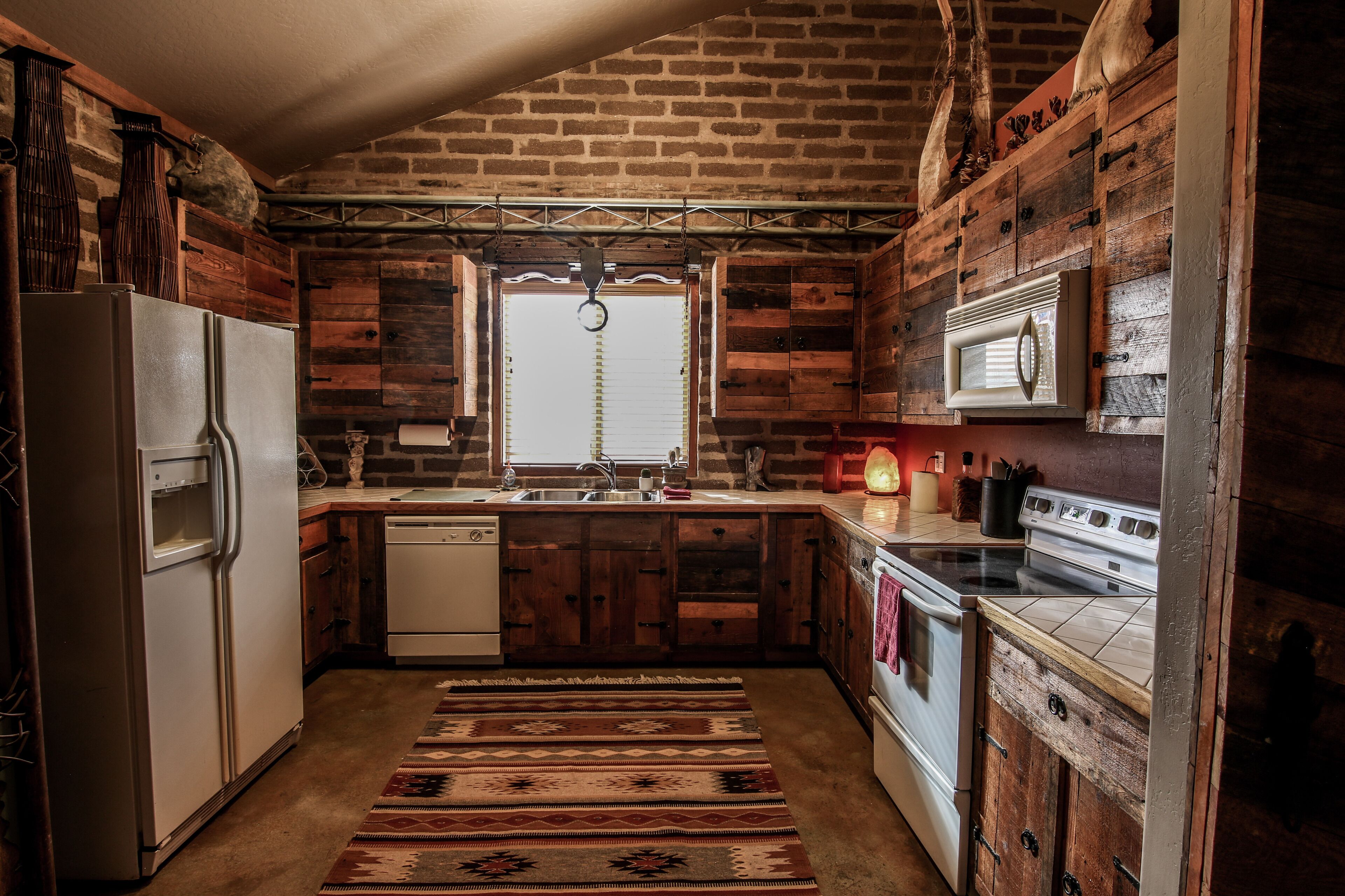 A rustic kitchen with wooden walls, a brick ceiling, a refrigerator, a dishwasher, a stove, and a microwave.