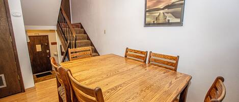 Un comedor con una mesa y sillas de madera, una escalera y un cuadro en la pared.