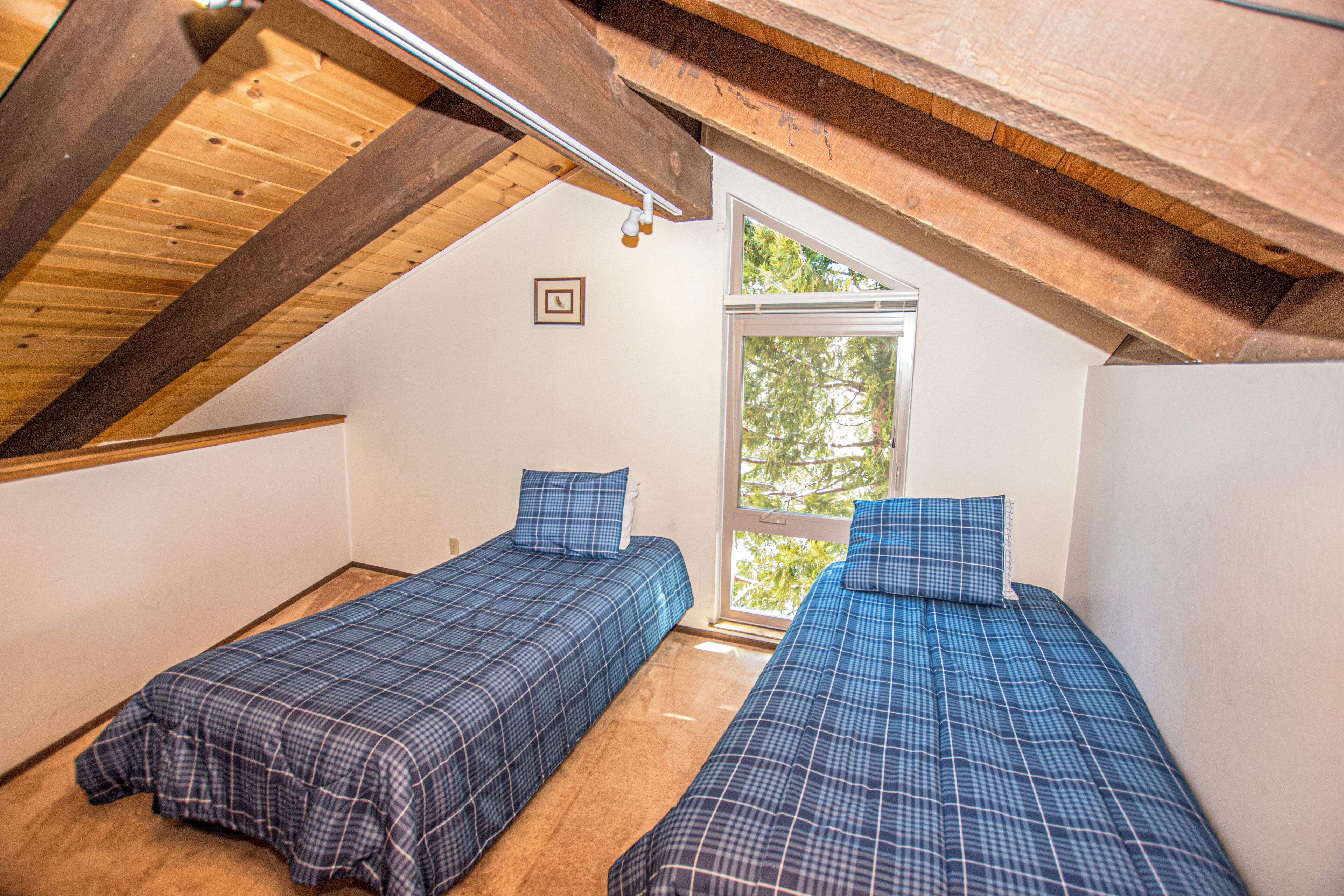 Una habitación con dos camas, vigas de madera, un ventanal y una puerta.