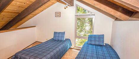 Una habitación con dos camas, vigas de madera, un ventanal y una puerta.
