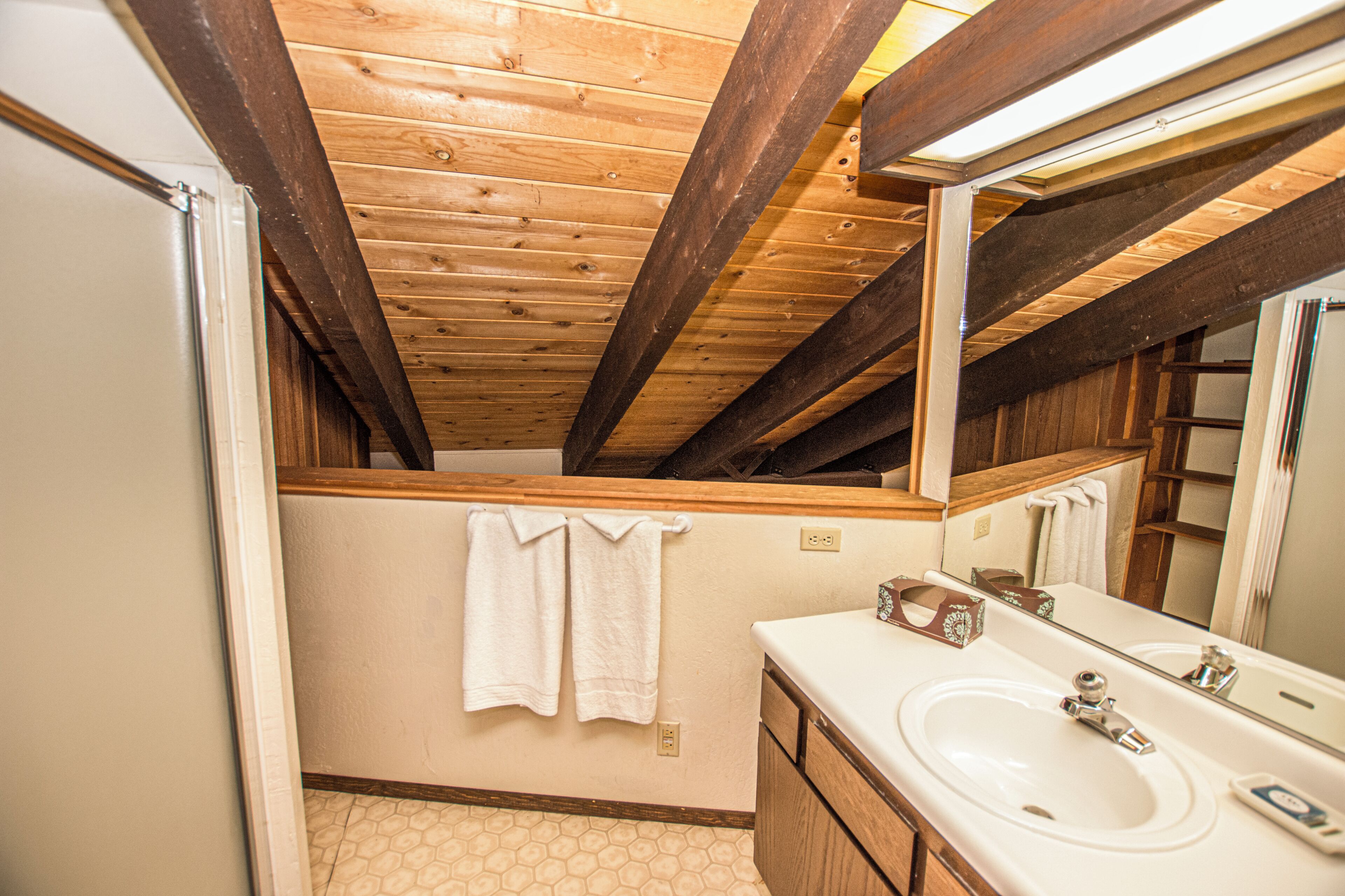 Een badkamer met houten balken, een witte wastafel en een grote spiegel.