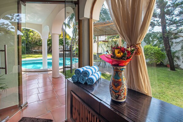 A room with a view of a pool, a vase with flowers, and rolled towels on a table.