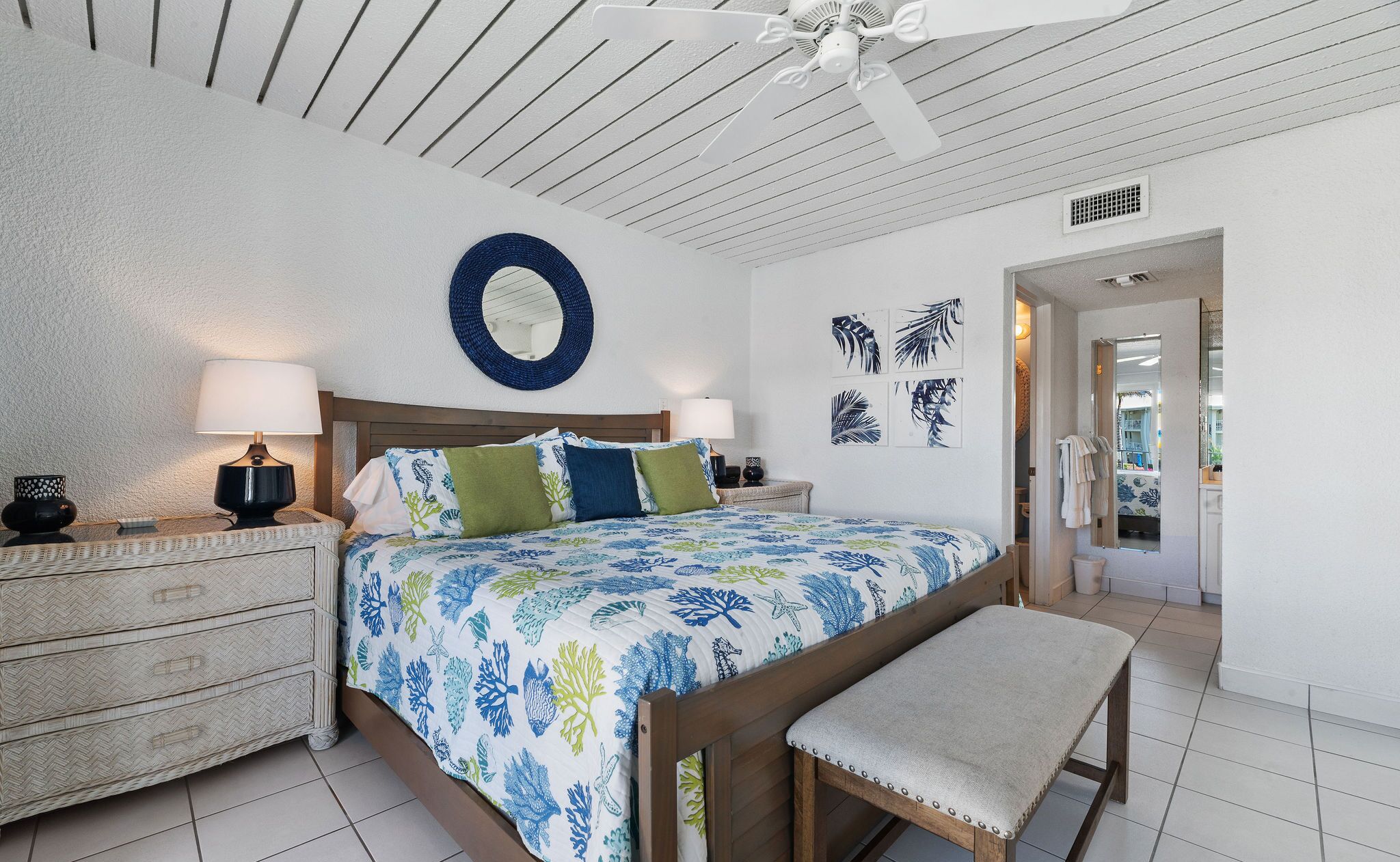 Ein Schlafzimmer mit einem Bett, zwei Nachttischen, einer Bank, einem Deckenventilator und Wandbildern.