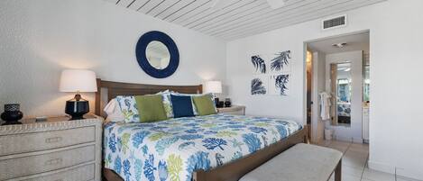 Ein Schlafzimmer mit einem Bett, zwei Nachttischen, einer Bank, einem Deckenventilator und Wandbildern.