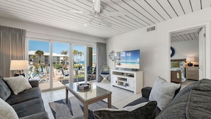 A modern hotel room with a balcony, a flat-screen TV, and a seating area with a glass coffee table.