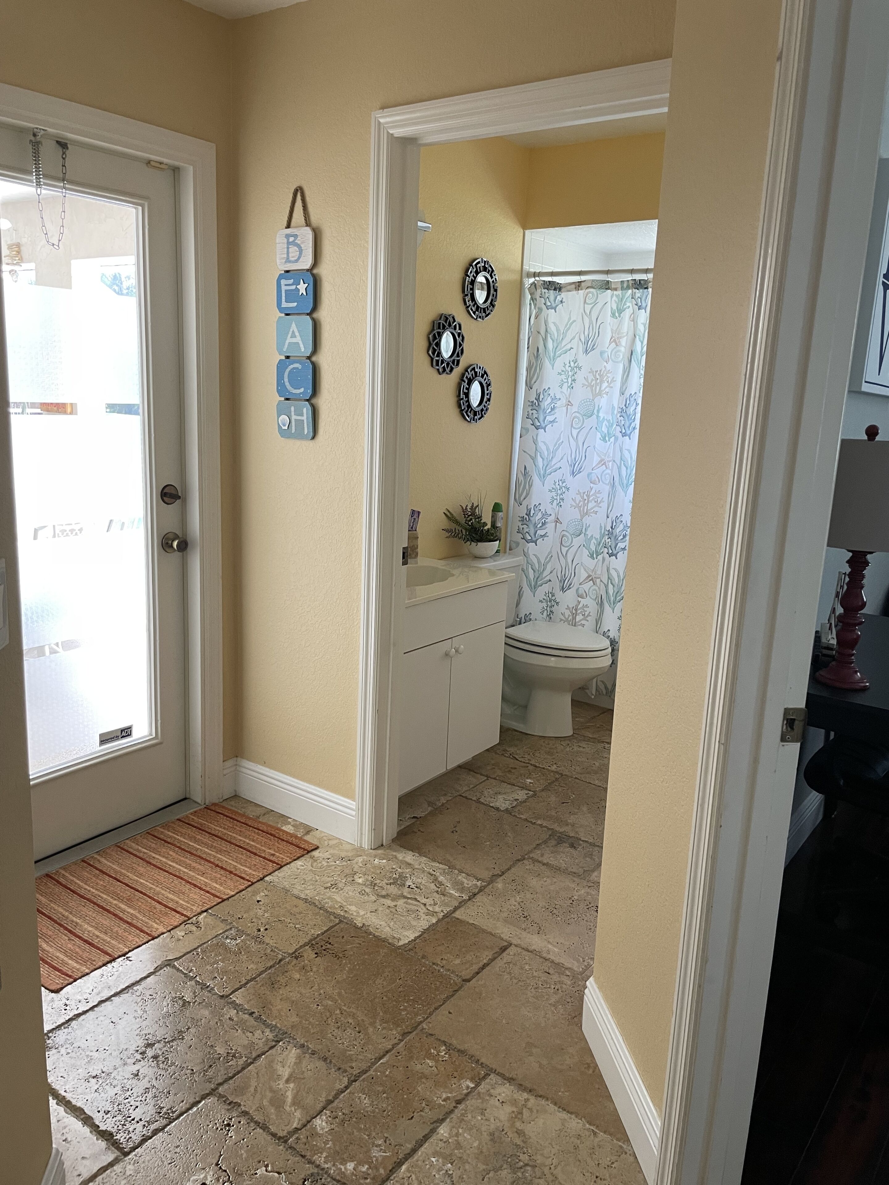 A bathroom with a toilet, sink, and decorative mirrors. There is a door with a doormat and a wall-mounted sign.