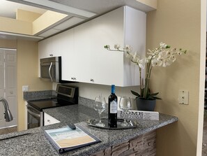 Una cocina con armarios blancos, encimera de granito, una botella de vino y un cartel de bienvenida.