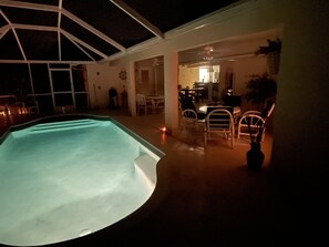 Una piscina interior con techo de vidrio, rodeada de sillas blancas y una mesa de comedor.