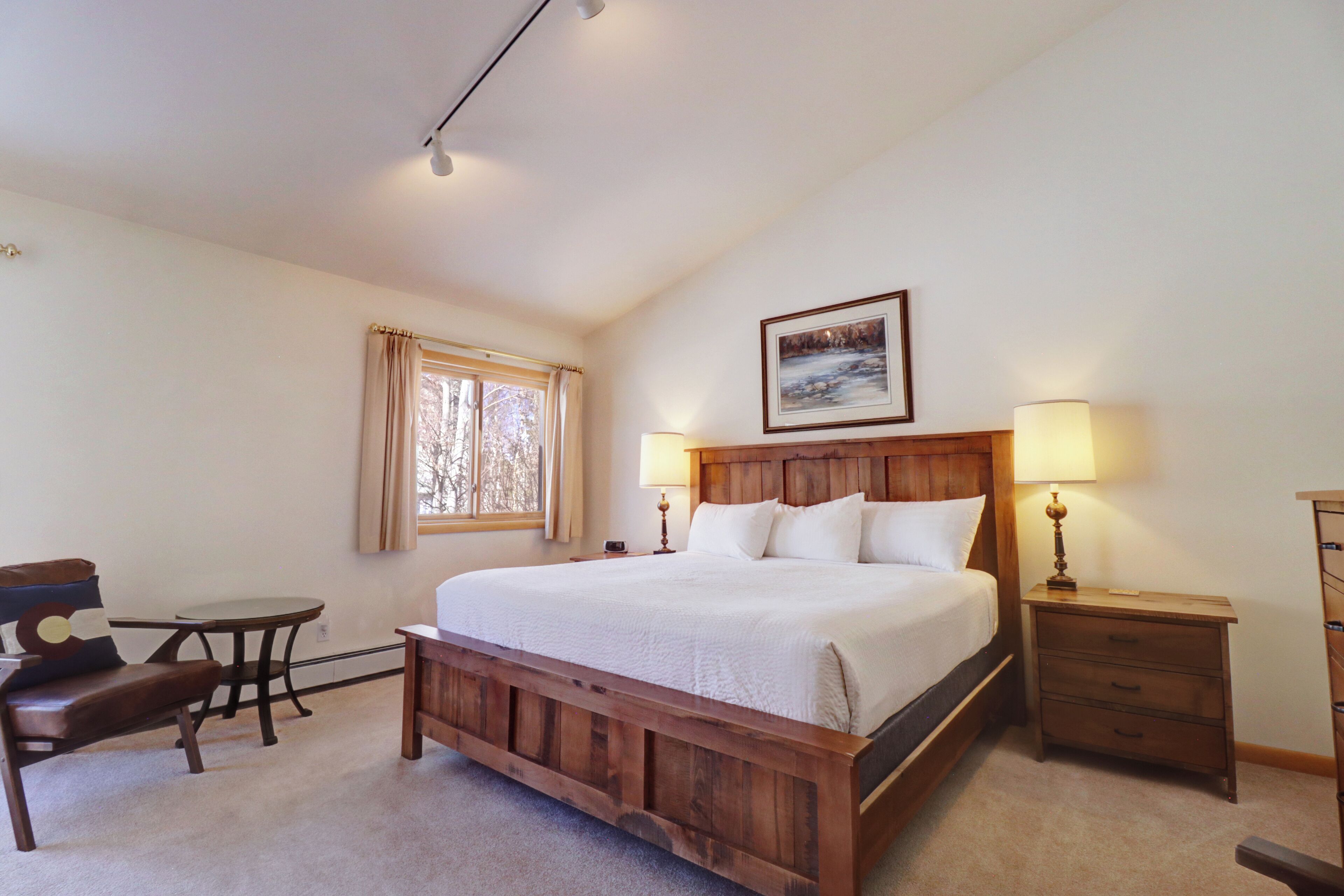 A bedroom with a wooden bed, bedside tables, a chair, a window, and a painting on the wall.