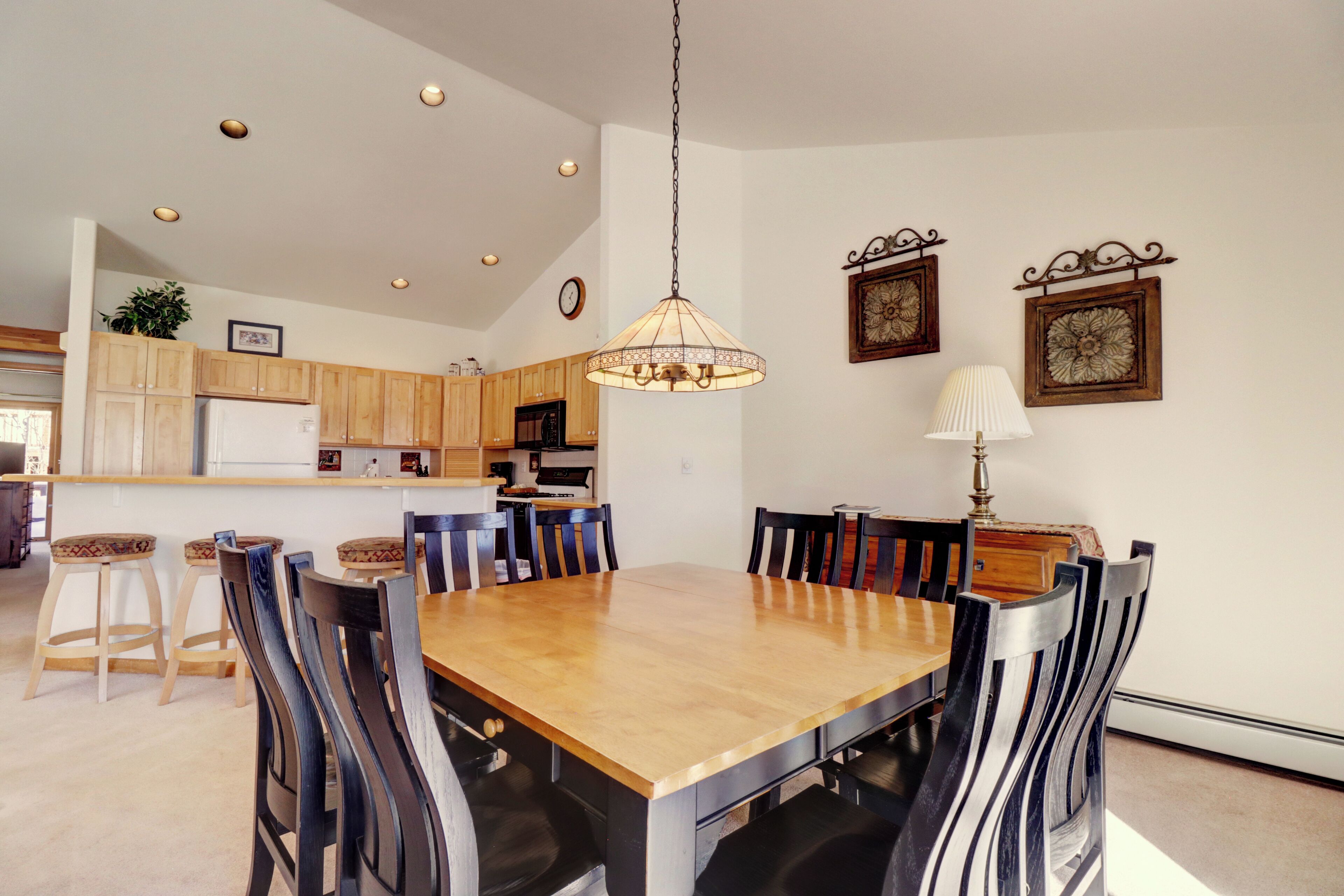 Un coin repas avec une table et des chaises en bois, un luminaire suspendu et des meubles de cuisine en arrière-plan.