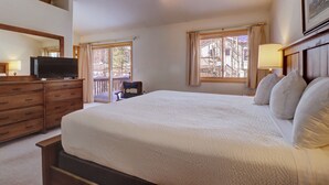 A hotel room with a large bed, wooden dresser, television, and a balcony with a chair.