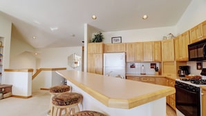 A modern kitchen with wooden cabinets, a central island with stools, a refrigerator, stove, and a microwave.