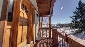 A wooden deck with a wooden door and windows, leading to a snowy landscape with trees and buildings in the background.