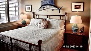 Un dormitorio con cama, dos mesitas de noche, una escultura de pez montada en la pared y dos cuadros enmarcados.