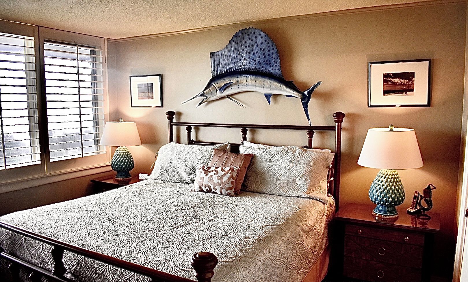 Une chambre à coucher comprenant un lit, deux tables de chevet, une sculpture de poisson fixée au mur et deux tableaux encadrés.