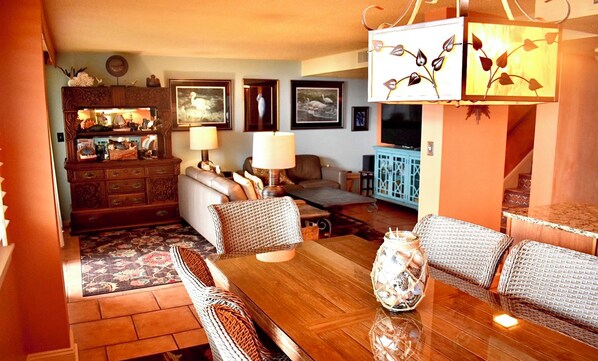 A cozy living room with a wooden dining table, wicker furniture, and a decorative lamp.