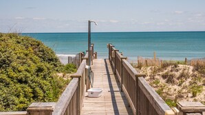En träpromenad som leder till en strand med kristallklart blått vatten.