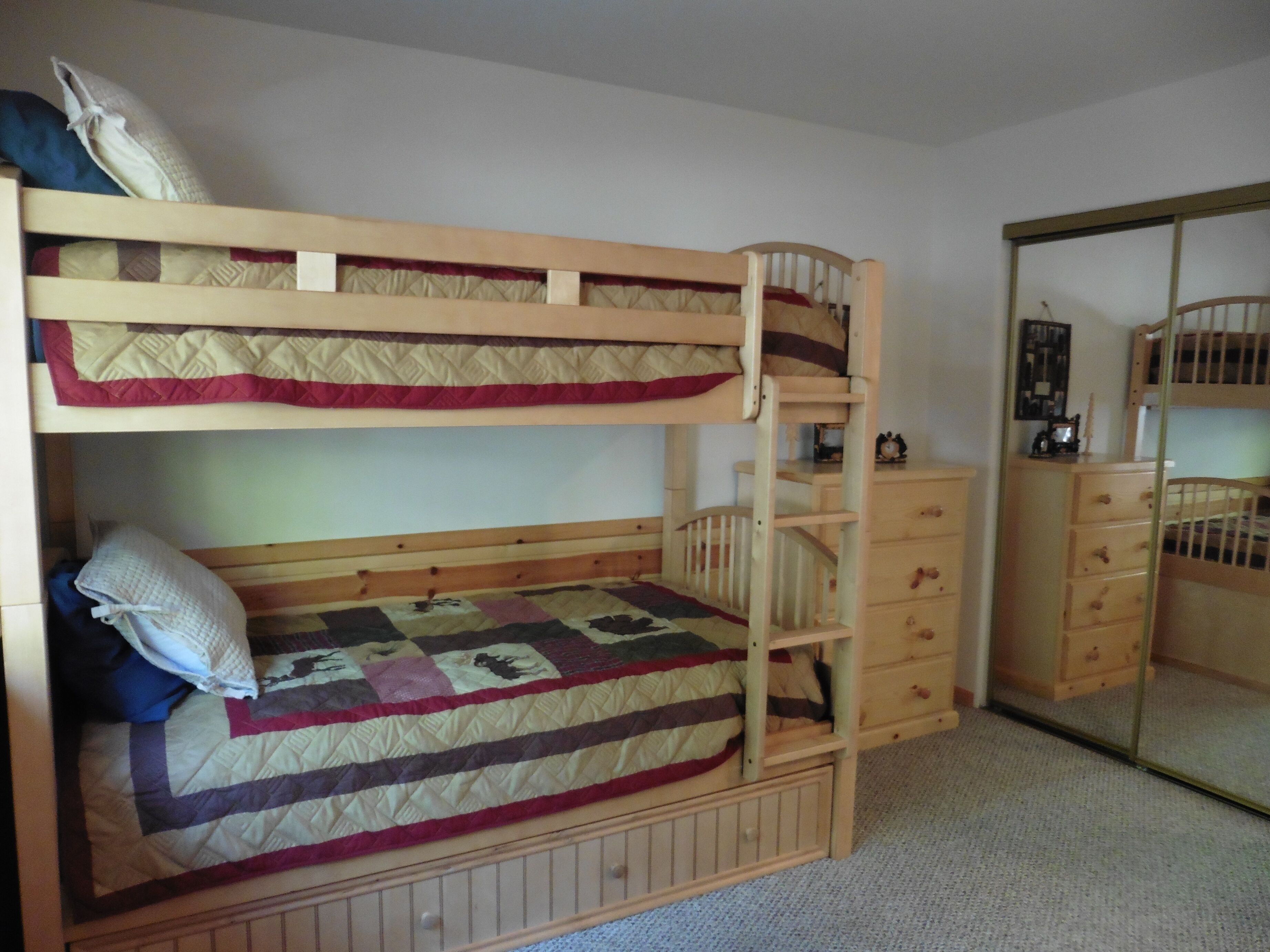 Una cama litera con colchón acolchado y una cómoda de madera con cajones.