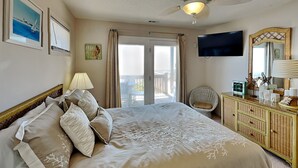 Ein Hotelzimmer mit einem großen Bett, einem Fernseher, einem Schminktisch und einem Balkon mit Blick.