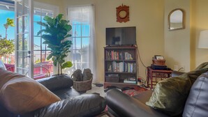 Uma sala de estar com uma planta grande, estante de livros, televisão e janela com vista.