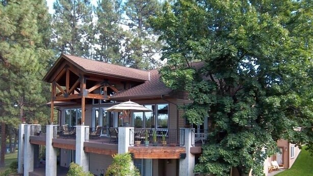 A multi-level wooden cabin with a balcony, surrounded by lush greenery and trees. - Riverfront Lodge great setting, walk to downtown! (Bend)