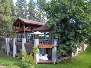 A multi-level wooden cabin with a balcony, surrounded by lush greenery and trees. - Riverfront Lodge great setting, walk to downtown! (Bend)