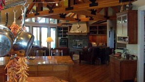 A spacious kitchen with wooden beams, a fireplace, and a dining area with a large window. - Riverfront Lodge great setting, walk to downtown! (Bend)